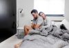 Couple sitting on bed in pijamas with problem so he is upset while she try to confort him