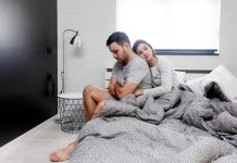 Couple sitting on bed in pijamas with problem so he is upset while she try to confort him